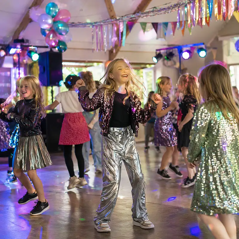 Kinderen dansen en spelen tijdens een indoor kinderfeestje met disco verlichting in een feestzaal
